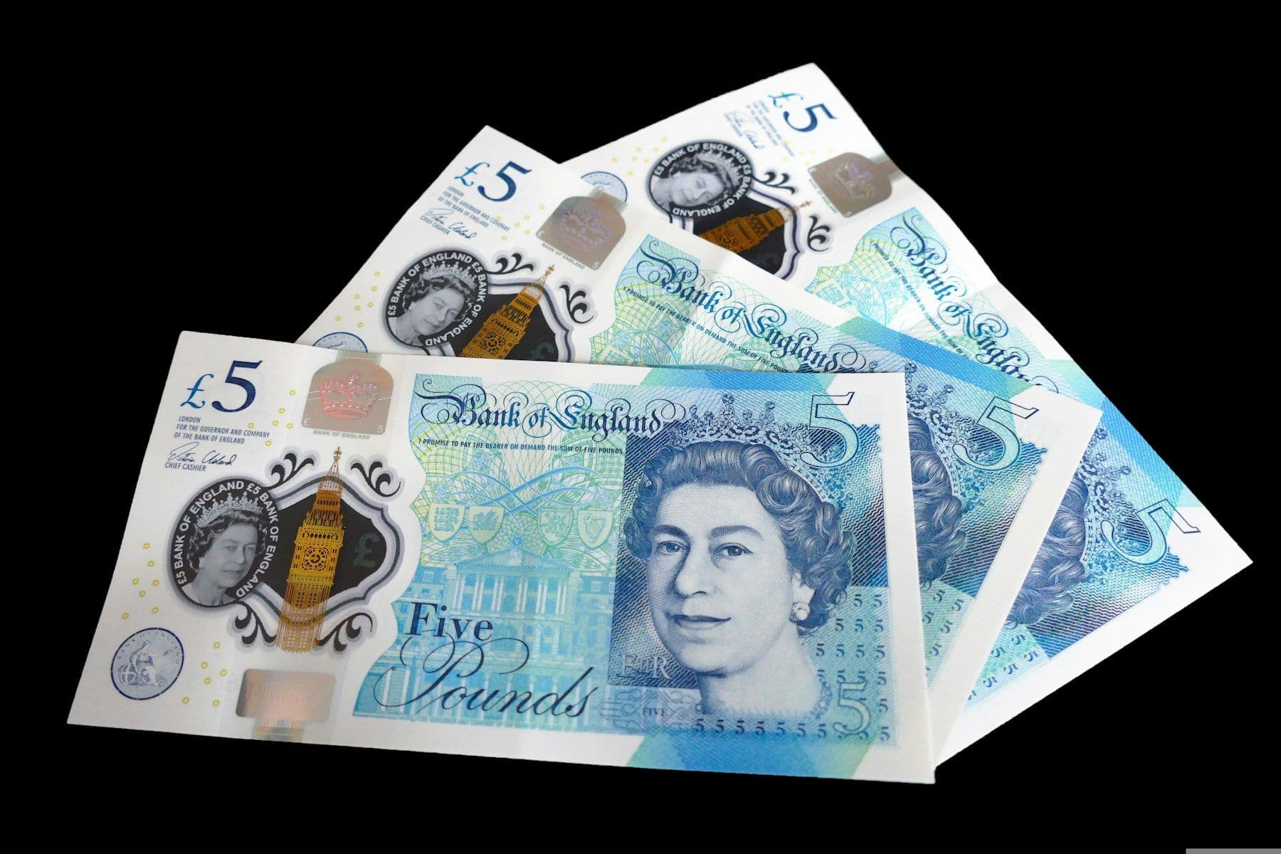 A fan of British five pound notes on a black background